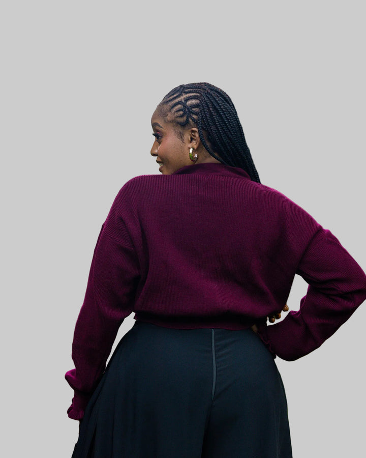 Person wearing a burgundy sweater and dark pants standing outdoors with trees in the background