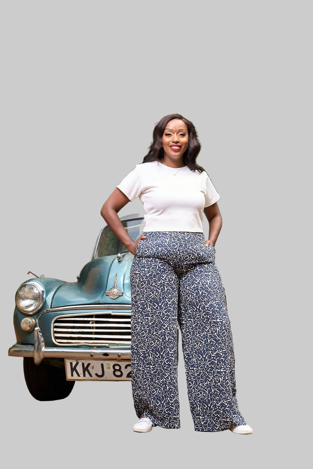Woman standing in front of a vintage car with greenery in the background