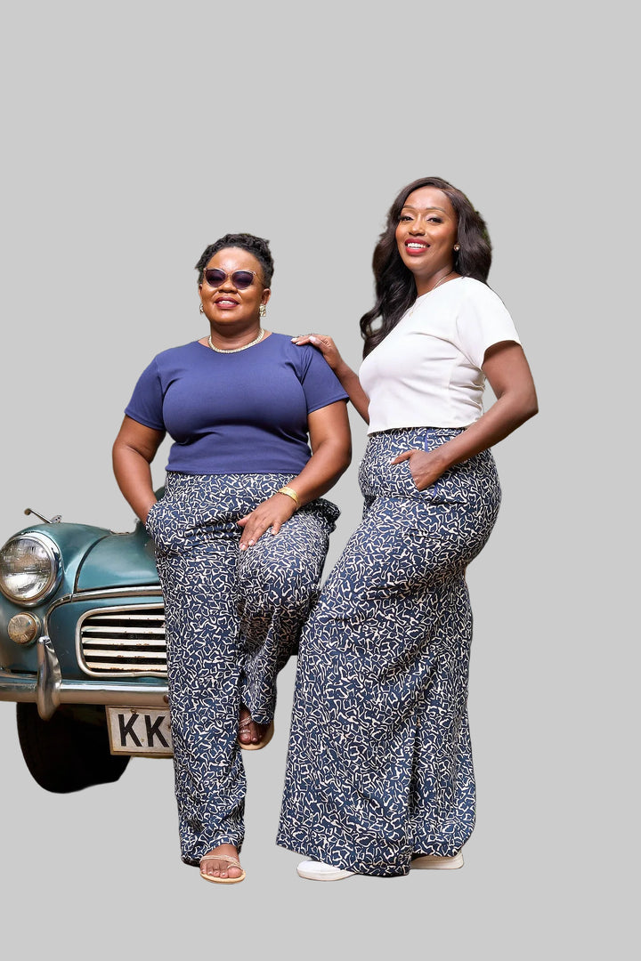 Two women posing in front of a vintage car with greenery in the background