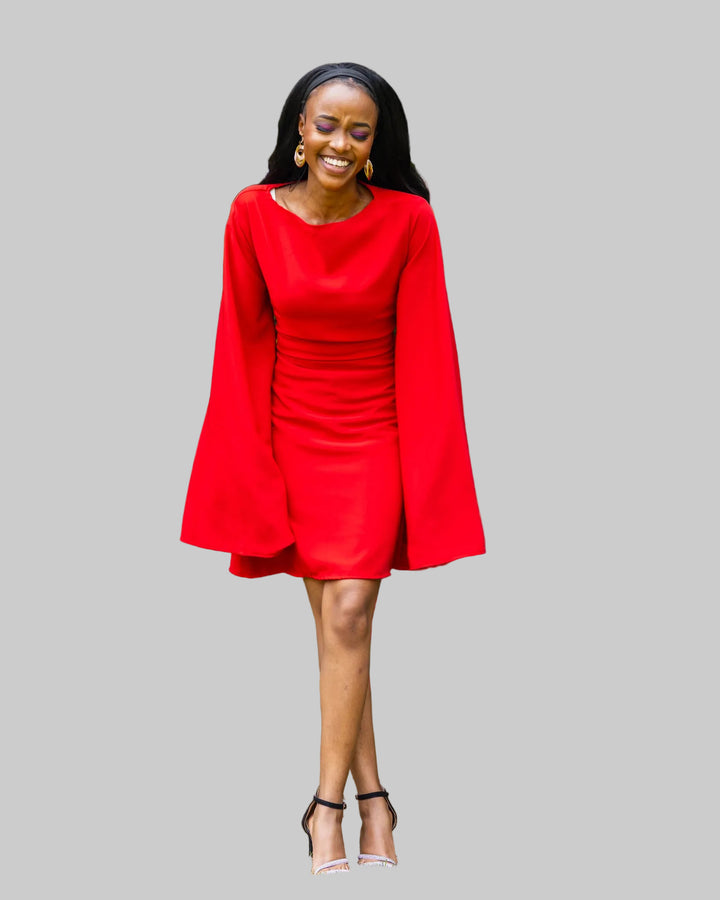 Woman in a red dress standing outdoors with greenery in the background