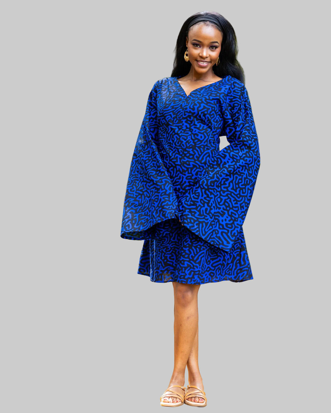 Woman wearing a blue dress standing outdoors with greenery in the background