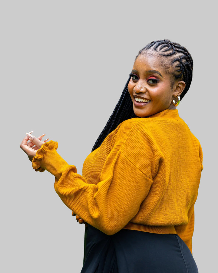 Woman in a mustard yellow sweater with braided hair standing outdoors.